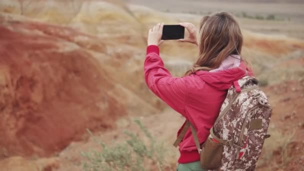 Meisje toeristische maakt foto's op de camera smartphone. rode bergen en rode aarde als op Mars. — Stockvideo