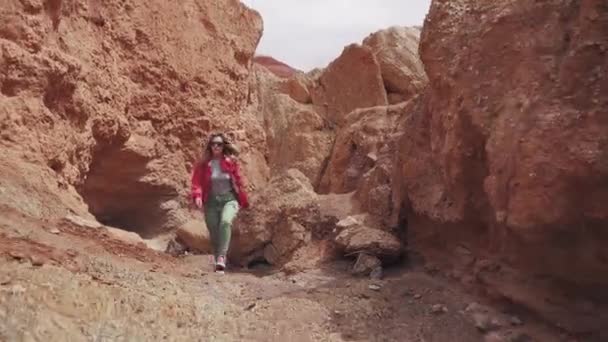 Τουριστικό είναι το περπάτημα κατά μήκος ορεινά εδάφη. νεαρή γυναίκα ταξιδιώτη με σακίδιο. κόκκινη γη και βουνά, όπως στον Άρη — Αρχείο Βίντεο