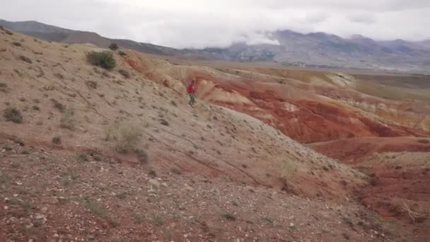 旅行者下山。一个带着背包的旅游女孩戴着太阳镜沿着山地的地形行走. — 图库视频影像