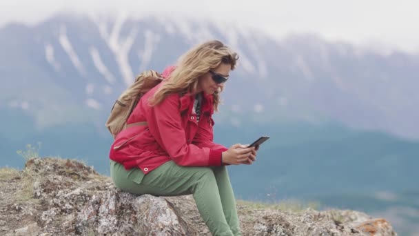 Ταξιδιώτης χρησιμοποιεί ένα smartphone χαλαρώνοντας στα βουνά. κορίτσι τουριστικά κατέχει ένα κινητό τηλέφωνο — Αρχείο Βίντεο