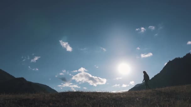 Silueta de un viajero en el fondo de las montañas y el cielo. la chica turista está caminando por la cima de la colina — Vídeos de Stock