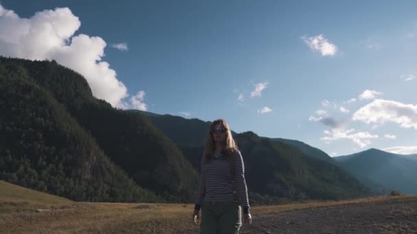 Bir turist kız yakın çekim portresi. Bir gezgin bir sırt çantası ve dağlık arazi giyen güneş gözlüğü yürür. — Stok video