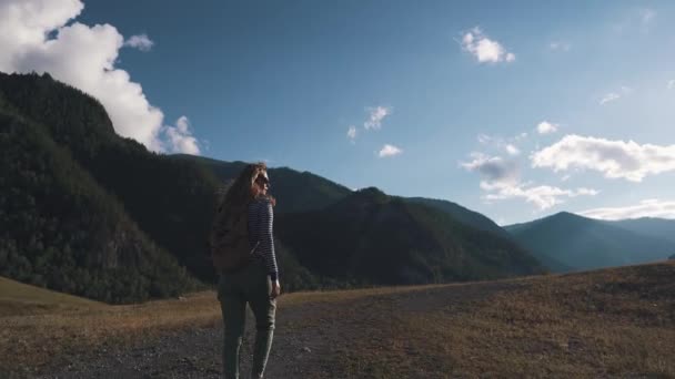 Ritratto di una ragazza turistica primo piano. Un viaggiatore con uno zaino e occhiali da sole cammina attraverso il terreno montagnoso . — Video Stock