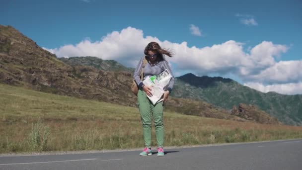 Turisztikai lány nem tud megbirkózni a papír térképet az erős szél miatt. nő utazó egy hátizsák és a Térkép a kezében — Stock videók