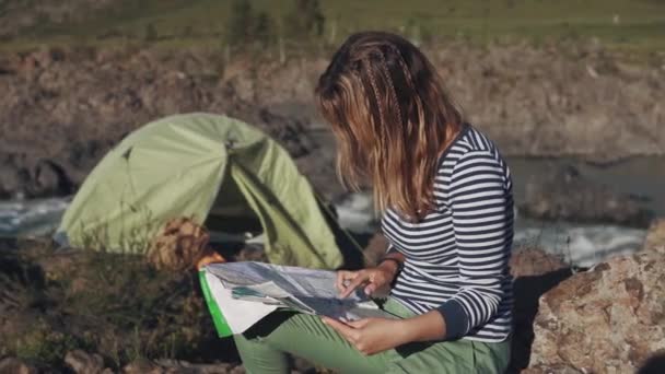 Ung kvinna traveler håller en papperskarta. turist i bakgrunden i ett tält i bergen — Stockvideo