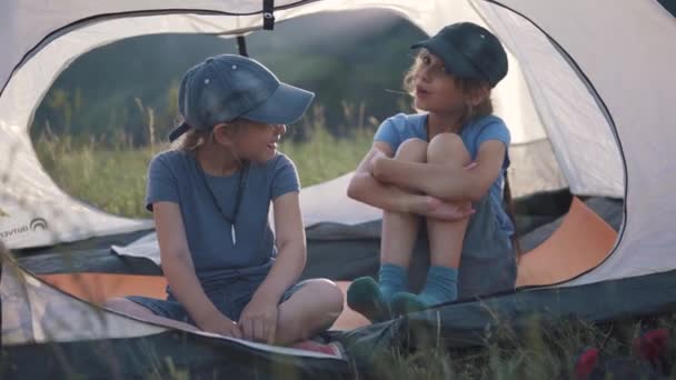 Enfants bavardent joyeusement tout en étant assis dans une tente à l'extérieur. deux petites filles voyageur — Video