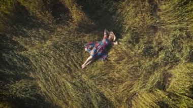 Ellerini başının arkasına ile çim üzerinde yalan aerial.girl. güzel bir kadın samanlıkta rustik bir elbise içinde. yukarıdan görüntülemek.
