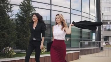 mutlu ve memnun iş kadınları sokakta yürürken eğlenin. iş adamları başarılı bir hareket ile mutluyuz. Kız onun ceketi boyundan büyük sallıyor