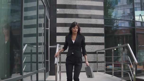 Atractiva mujer de negocios sale de un moderno centro de negocios y camina con confianza por la calle — Vídeos de Stock