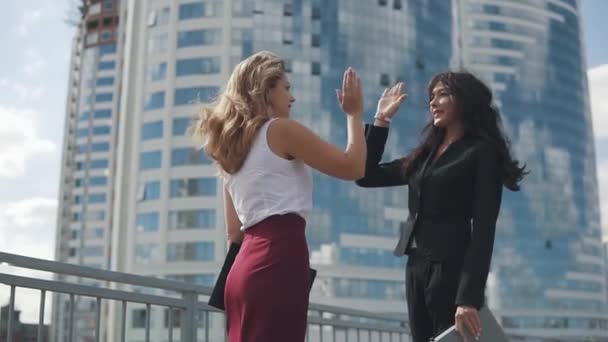 Concept of success in business relations. satisfied business women give each other five and smile happily. portrait of girls in strict suits against the backdrop of a business center — Stock Video