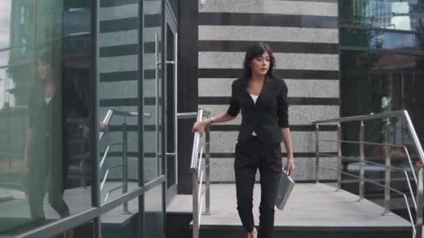 Hermosa mujer de negocios en un traje estricto y con una carpeta de papeles va cerca del centro de negocios — Vídeos de Stock