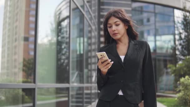 Chica atractiva en un traje de negocios utiliza un teléfono inteligente. joven mujer de negocios mensajes de texto un mensaje en un teléfono móvil — Vídeos de Stock