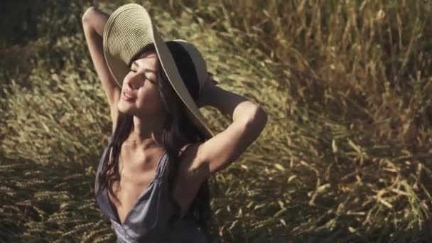 Retrato de cerca de una joven hermosa mujer atractiva en un sombrero de paja en un campo al atardecer — Vídeos de Stock