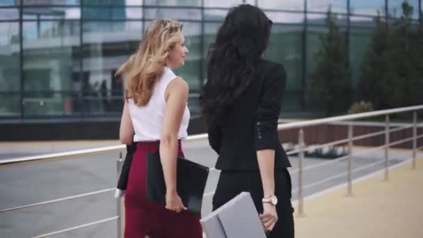 ビジネスの女性は、ビジネス センターでは論文のためのフォルダーの背景に対して行きます。厳格なスーツを着た 2 人の女の子。背面図 — ストック動画