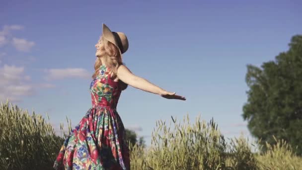 Roztomilá mladá žena ve slamáku se usmívá a víry, drží slaměný klobouk. Portrét atraktivní dívka s krásným úsměvem v pšeničné pole. Zpomalený pohyb — Stock video