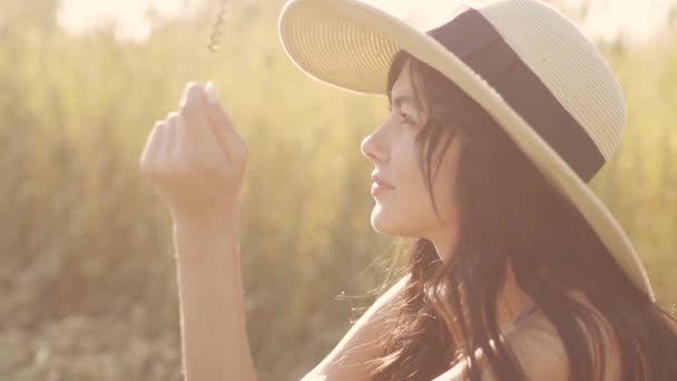 Retrato de cerca de una chica sentada en un prado y disfrutando de un cálido sol al atardecer — Vídeos de Stock