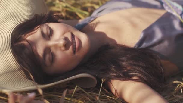 Hermosa chica se encuentra con los ojos cerrados en un campo de trigo abre los ojos y sonríe a la cámara. retrato de primer plano — Vídeos de Stock
