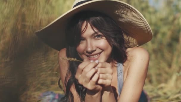 Ritratto ravvicinato di una giovane affascinante ragazza con un cappello di paglia. Una ragazza con occhi insoliti guarda e sorride alla macchina fotografica . — Video Stock