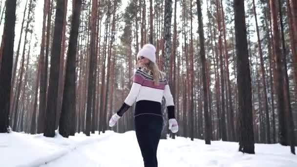 Girl in a sweater and hat on a walk in the winter forest and turns around at the camera. Back view — Stock Video