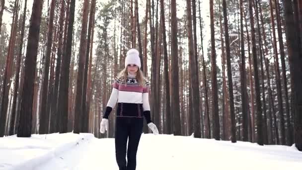 Chica alegre caminando por el bosque de invierno y sonriendo. Retrato de una joven con manoplas de jersey y sombrero — Vídeos de Stock