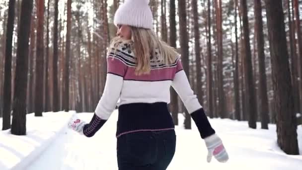Vrolijke zorgeloos meisje loopt door het bos van de winter en blikt terug op de camera. Jonge vrouw in een trui en een gebreide cap — Stockvideo