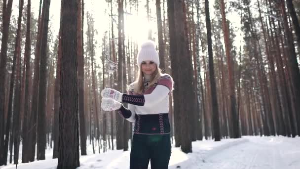 Девушка бросает снежок в камеру и улыбается. Портрет милой и беззаботной девушки в свитере и вязаной кепке. замедленное движение — стоковое видео
