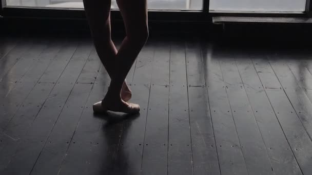 Benen av en ballerina i pointe skor närbild. Silhuetten av en ballerina mot bakgrund av ett stort fönster. slowmotion — Stockvideo