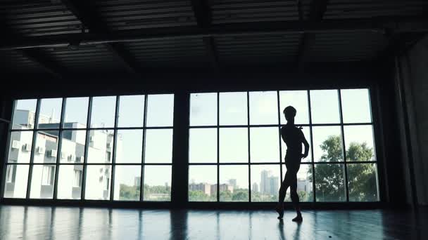 silueta muže baletní tanečnice tančí na pozadí velké okno. tanečnice tančí elegantně ve studiu. Zpomalený pohyb