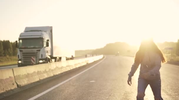 Mädchen Teenager Skateboarding auf einer menschenleeren Autobahn bei Sonnenuntergang. rothaariges Mädchen in zerlumpten Jeans und Kopfhörern — Stockvideo
