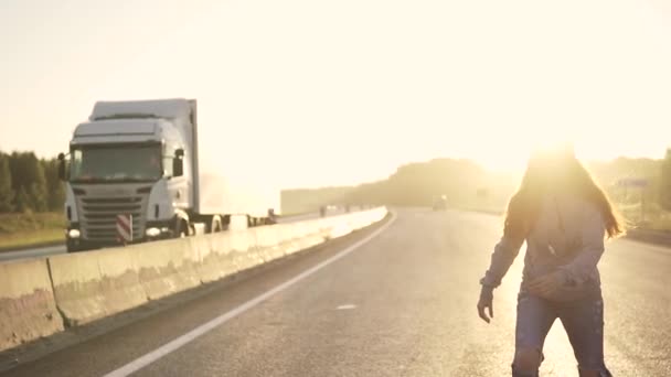 Flicka Tonåring skateboard på en öde motorväg vid solnedgången. Rödhårig flicka i trasiga jeans och hörlurar — Stockvideo