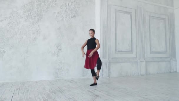 Een ballerina in zwarte bodysuits en een rode rok dansen in een ballet klas. Slow motion — Stockvideo