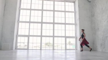 Balerin siyah bir gömlek ve kırmızı etek yüksek bir sicim Studio büyük bir ışık pencere karşı hava ile atlar. ağır çekim