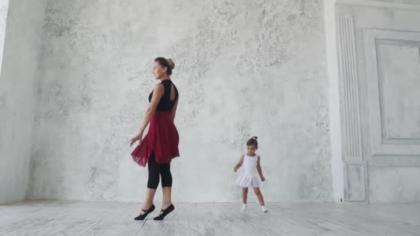 En liten rolig flicka försöker upprepa rörelserna bakom ballerinan i klassen balett. slowmotion — Stockvideo