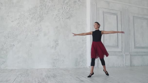 Μπαλαρίνα σε μαύρο κορμάκι και κόκκινη φούστα γυρίζει στις μύτες των ποδιών σε ανοιχτόχρωμο φόντο στο στούντιο. αργή κίνηση — Αρχείο Βίντεο