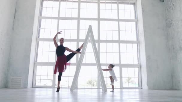 Een grappig meisje probeert te herhalen de bewegingen achter de ballerina in het ballet klas. Slow motion — Stockvideo