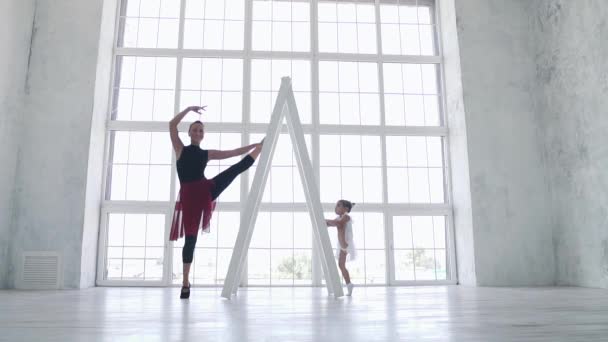 Маленькая забавная девочка пытается повторить движения за балериной в балетном классе. замедленное движение — стоковое видео