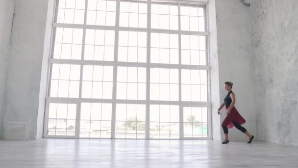 Bailarina en un body negro y una falda roja salta alto con un cordel en el aire en el estudio contra una gran ventana de luz. cámara lenta — Vídeo de stock