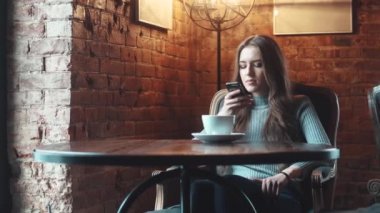 Genç çekici kız rahat bir kafede oturur ve bir cep telefonu kullanır