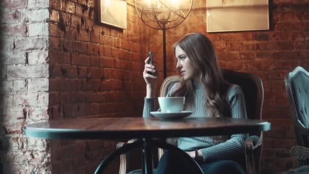 Retrato de una chica guapa en un café. chica hace selfie en cámara smartphone y bebidas café — Vídeos de Stock