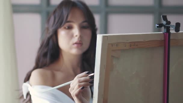 Attraktiva flicka målare målar en bild i en hemmastudio. konstnär med en pensel i handen — Stockvideo