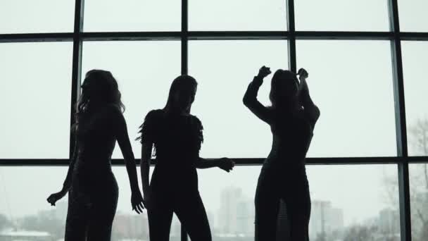 Meninas dançando no fundo de uma grande janela brilhante. silhuetas de pessoas divertidas — Vídeo de Stock