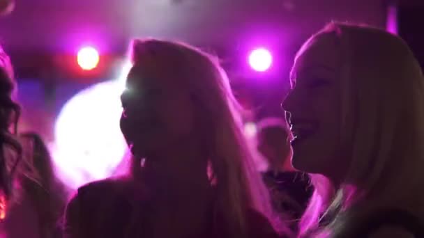 Barátnők táncol a tömegben az emberek a fénysugarak a dance club koncert spotlámpák — Stock videók