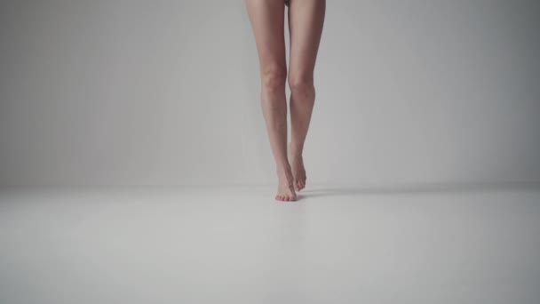 Vrouwelijke benen. meisje gaat op spitzen blote voeten op een witte achtergrond. — Stockvideo