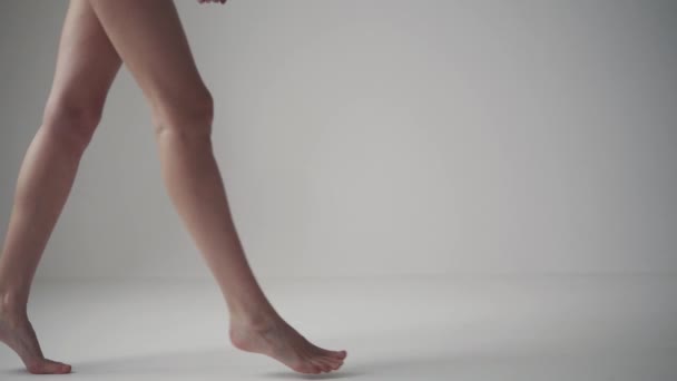 Kadın bacaklar. Kız uçlarında beyaz bir arka plan üzerinde yalınayak yürür. — Stok video
