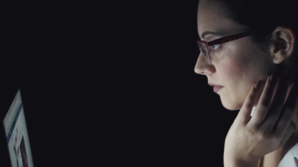 Porträtt av en ung kvinna spendera tid vid datorn i slutet av kvällen. flicka med glasögon som arbetar på en bärbar dator — Stockvideo