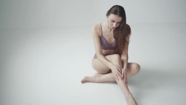 Девушка в кружевном белье сидит на полу. стройная девочка трогает ногу — стоковое видео