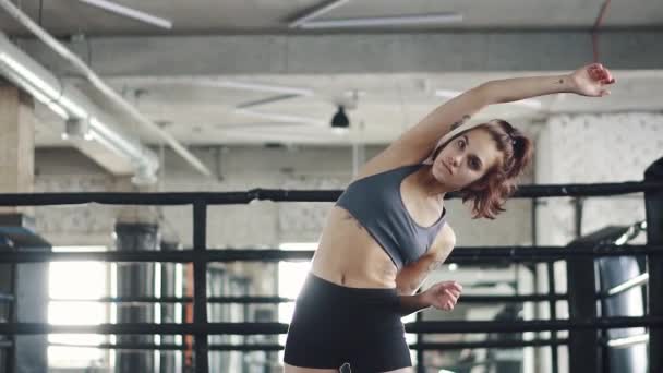 Retrato de una chica de fitness en el gimnasio. mujer joven con tatuaje se calienta contra el fondo del anillo de boxeo — Vídeos de Stock
