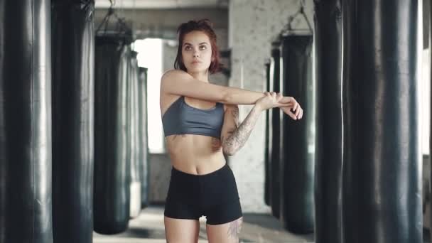 Κορίτσι μπόξερ ζέσταμα στο γυμναστήριο στο φόντο του εγκιβωτισμού τσάντες — Αρχείο Βίντεο