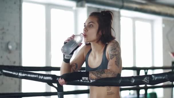 Девушка пьет воду в спортзале. девушка отдыхает после тренировки на боксерском ринге — стоковое видео