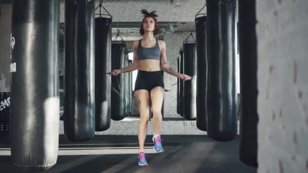 Дівчина робить кардіо. спортсмен стрибає мотузкою на фоні боксерських мішків — стокове відео